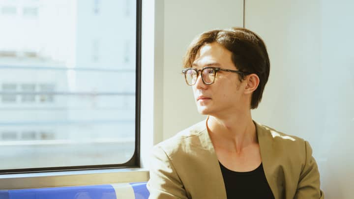 Young man with glasses gazes out a train window on a sunny day.