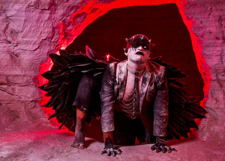 A fantasy character in dark costume emerges from a red-lit cave, creating a dramatic and surreal atmosphere.
