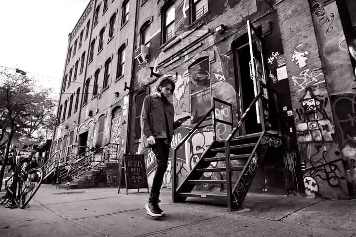Black and white photo of a person walking in Brooklyn's graffiti-filled street, showcasing urban art and architecture.