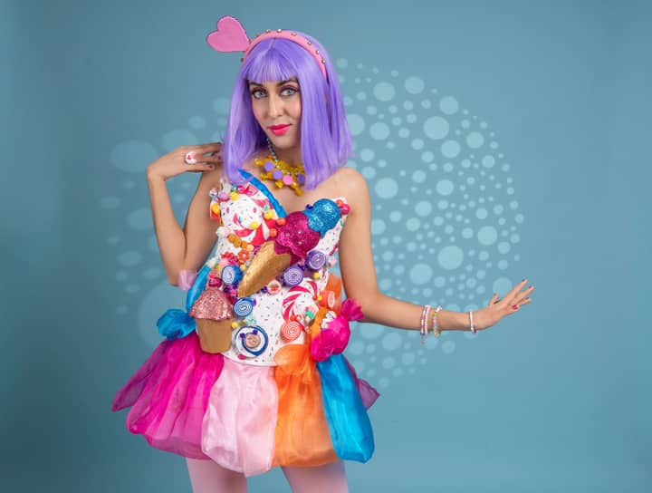 Colorful artistic cosplay woman in candy-themed costume on blue background.