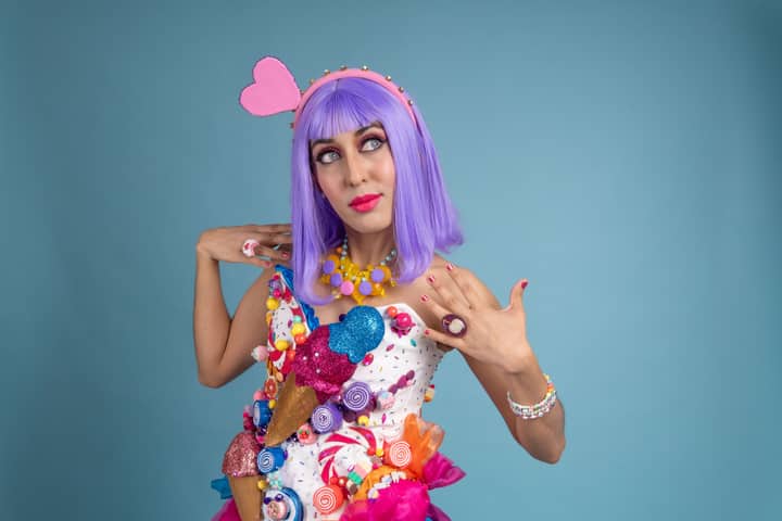 Colorful cosplay portrait of a woman in candy-themed attire against blue backdrop.