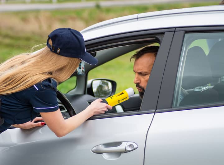 Police officer using breathalyzer to test driver's alcohol level outside car.