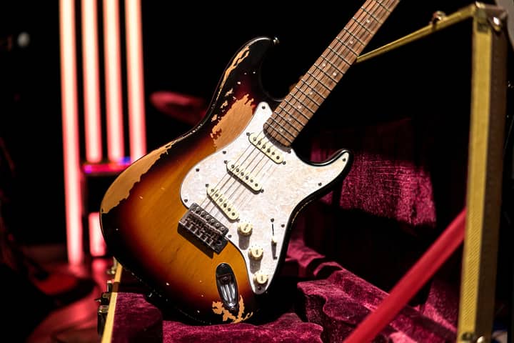 A vintage electric guitar with a sunburst finish showcased in a velvet-lined case under bright lights.