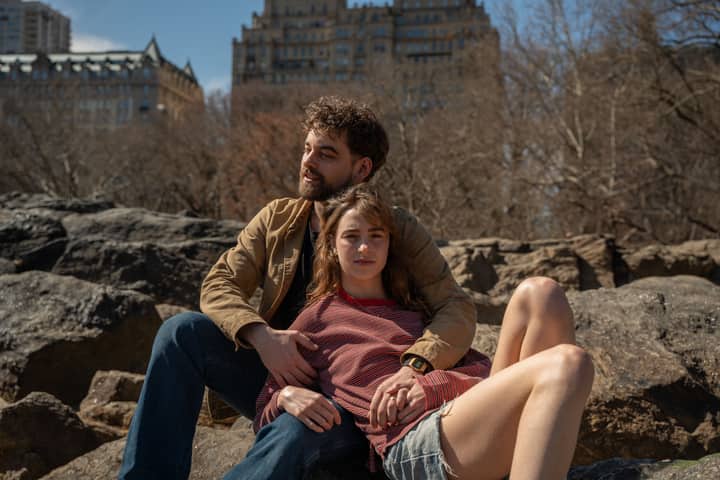 Couple enjoying a sunny day on Central Park rocks with city buildings in the background.