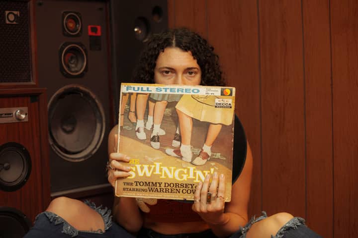 Person holding a vintage vinyl record in front of retro speakers, evoking a classic music ambiance.