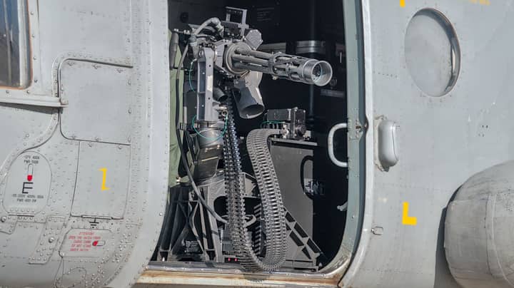 Close-up of a helicopter gun turret, showcasing detailed weaponry in bright sunlight.