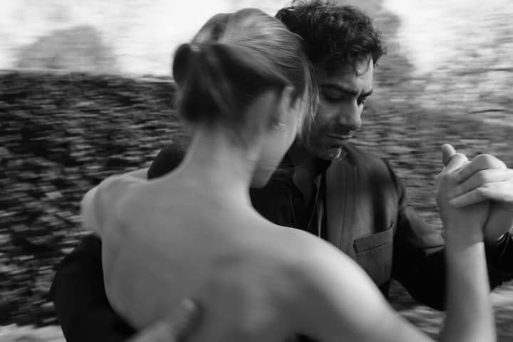 A couple gracefully dancing tango outdoors in a black and white photograph.