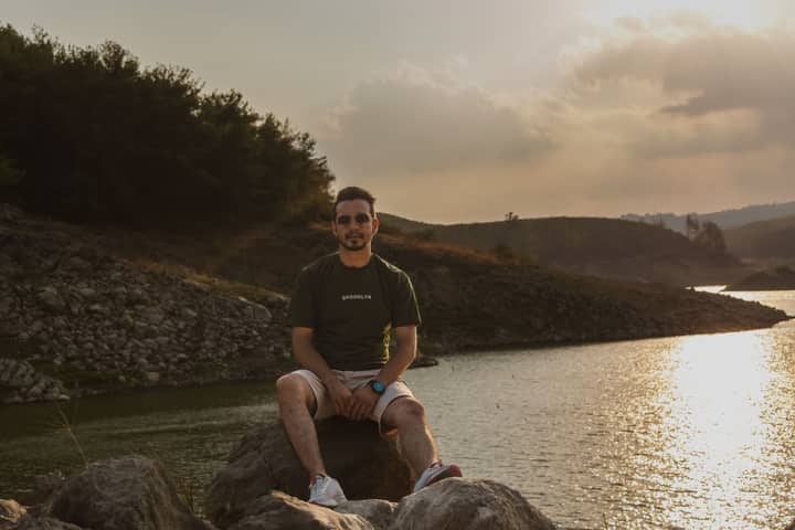 A man sits on rocks by a tranquil lake during sunset, exuding calmness and reflection. Ideal for relaxation and travel themes.