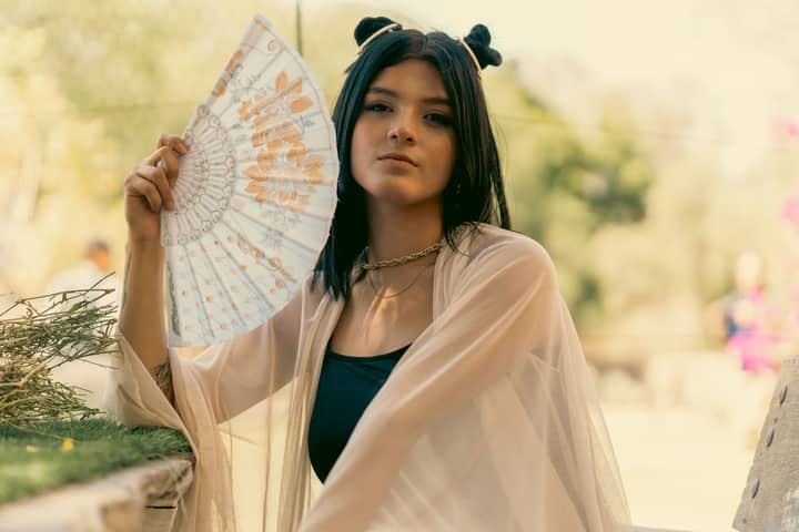 A young woman with a fan poses outdoors in Leon, Guanajuato, Mexico, exuding elegance.