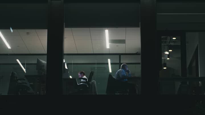 Two people working late in a modern Houston office building, visible through a window.