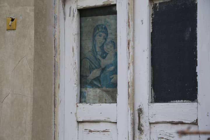 Weathered door with religious artwork and crackled paint, offering vintage charm.