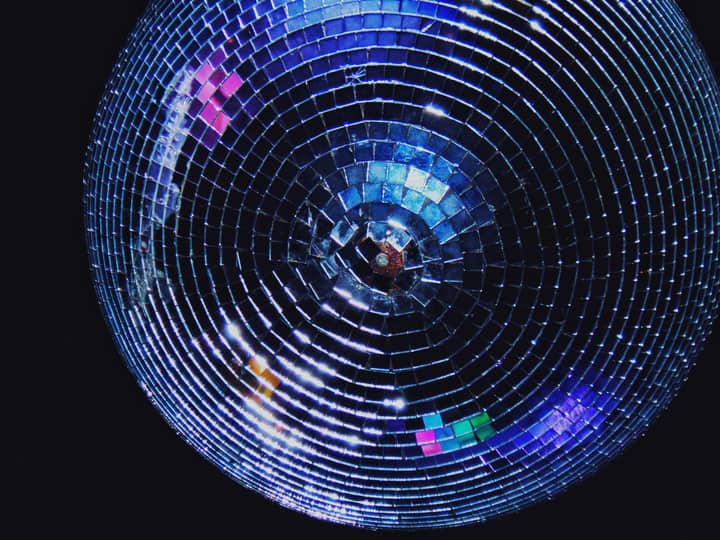 Close-up of a sparkling disco ball reflecting colorful lights in the dark, capturing a party atmosphere.