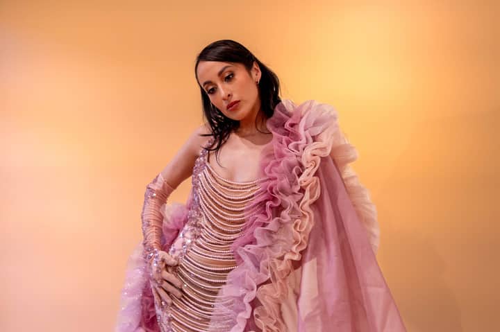 A woman in a pink ruffled dress posing against a warm background, exuding elegance and style.