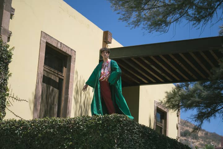 A person in a vibrant kimono poses elegantly outdoors against an architectural backdrop.