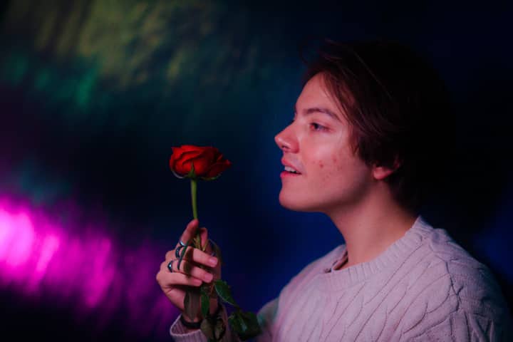 Side profile of a young person admiring a red rose, set against a vibrant and colorful background.