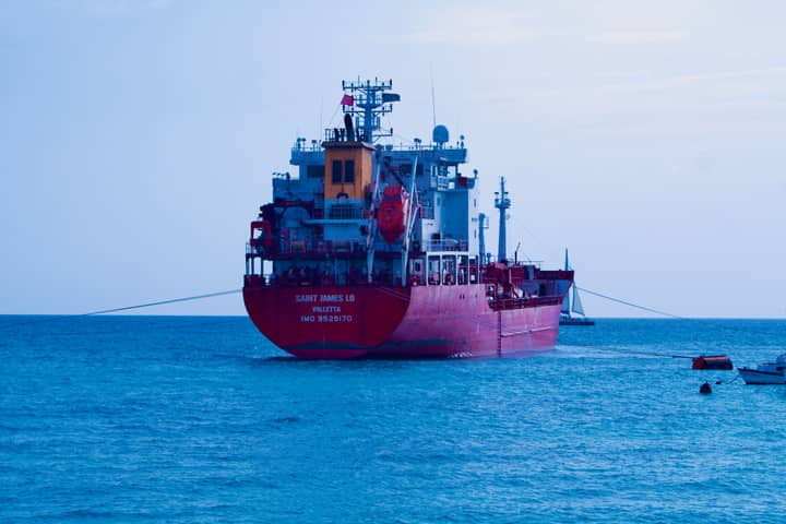 A red cargo ship sails in the calm blue ocean under a clear sky.
