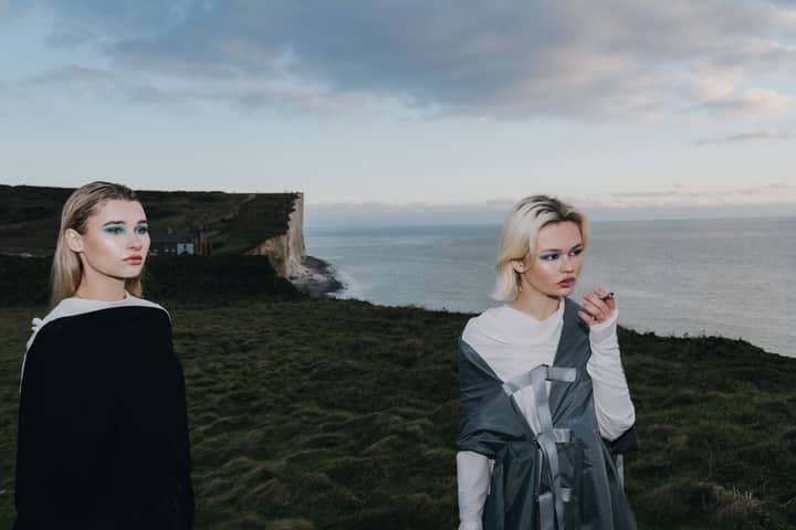 Two women with distinct style and makeup on a coastal cliff with sea view.