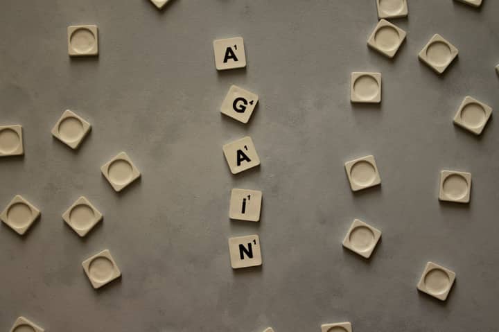 Top view of alphabet tiles spelling 'Again' on a neutral gray surface, surrounded by empty tile holders.