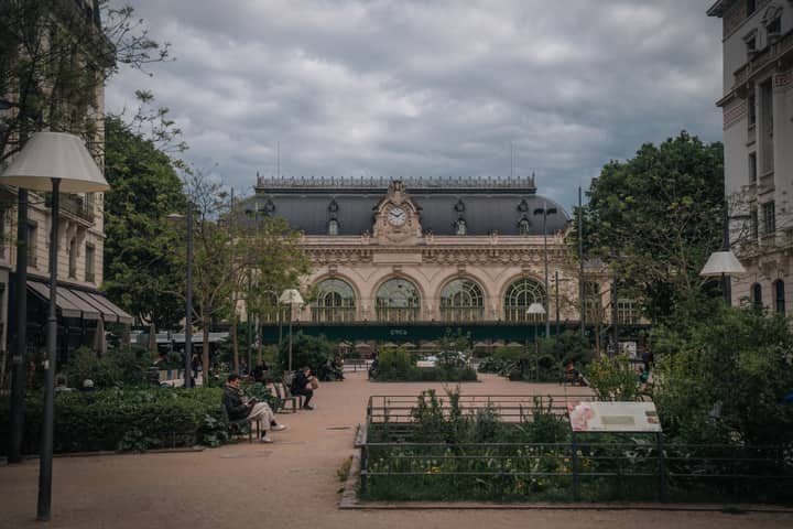 Scenic view of a European train station with historical architecture and lush greenery.
