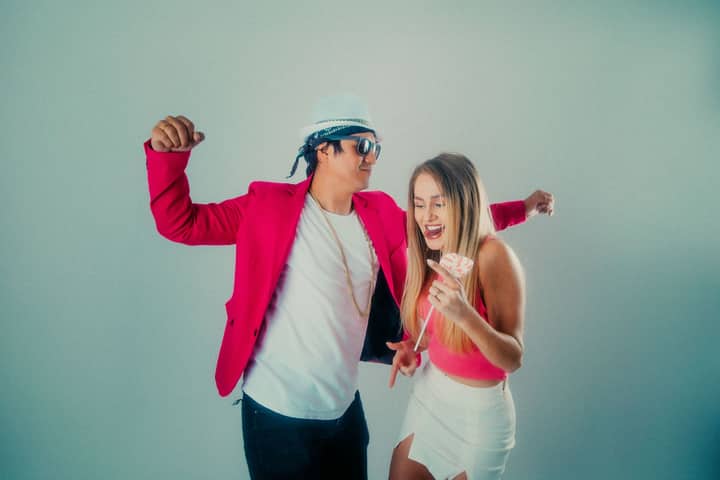 A lively couple dancing indoors, dressed in stylish pink attire, exuding joy and energy.