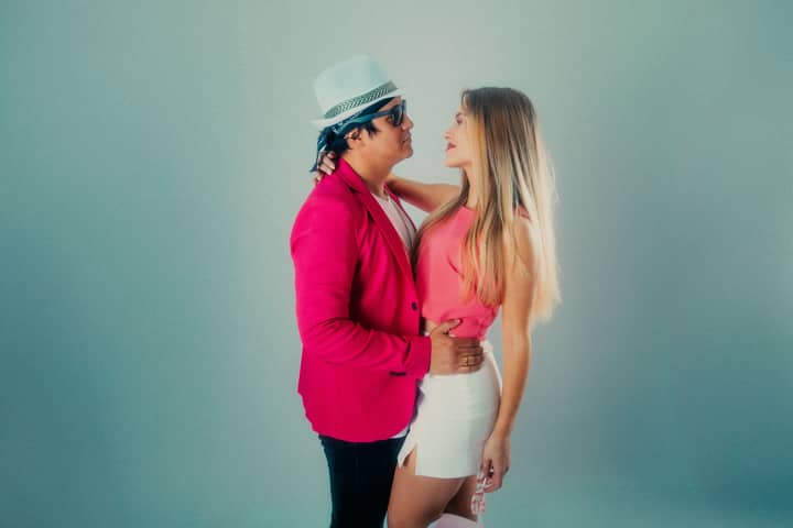 Elegant couple posing stylishly, wearing pink outfits against a neutral background.