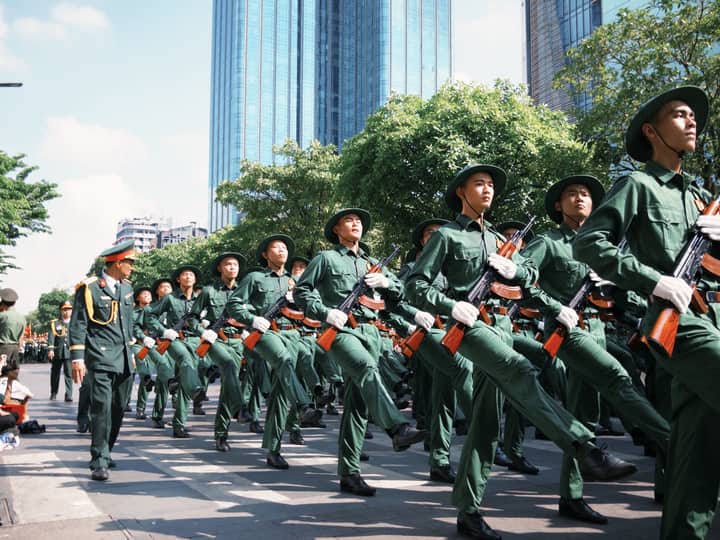 Marching soldiers in green uniforms participate in a city military parade.