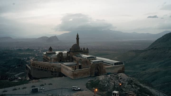 Aerial view of Işak Pasha Palace amid mountain landscape under cloudy skies.
