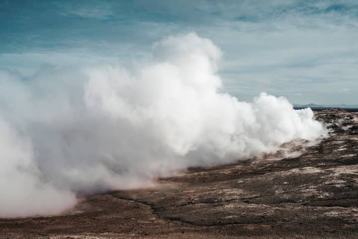 Majestic geothermal steam venting from Icelandic terrain on a clear day.