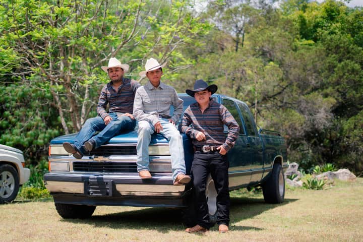 Three men in cowboy hats pose with a pickup truck on a sunny outdoor day.