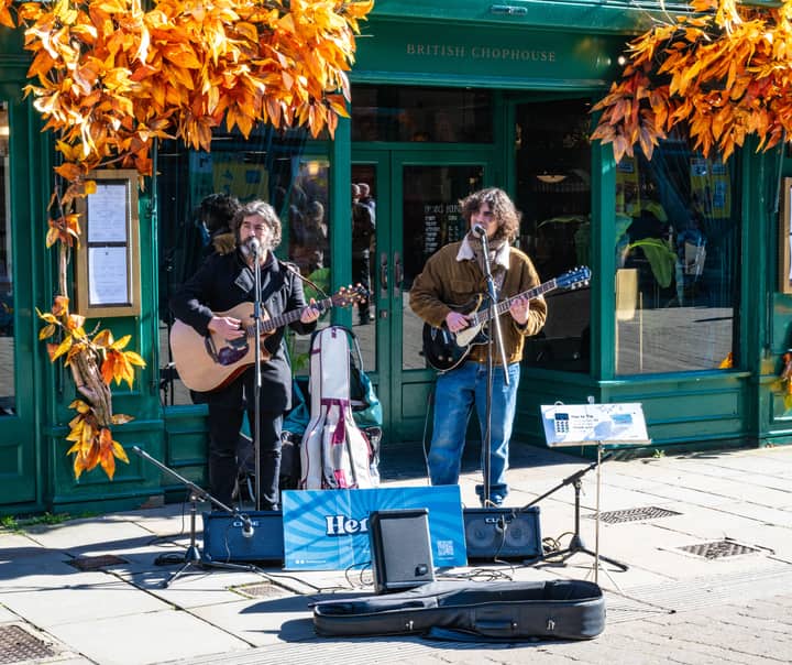 Two street musicians performing outside a decorated British chophouse in autumn.