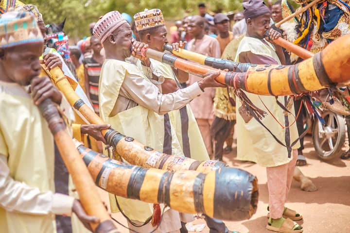 Colorful celebration with musicians playing traditional African horns at an outdoor cultural festival.