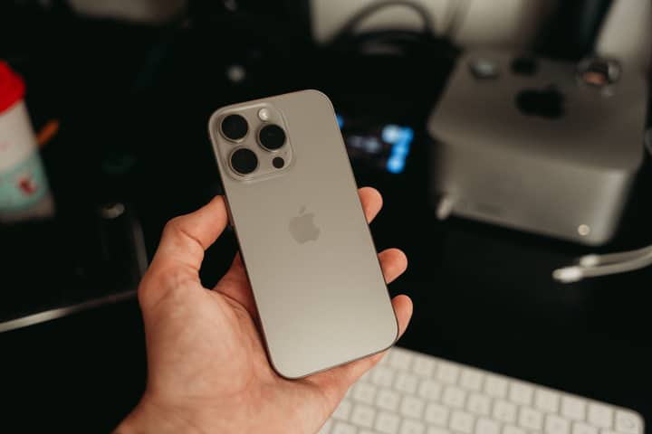 A hand holding a sleek smartphone in a tech-savvy office environment, showcasing its design.