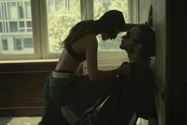 A dramatic urban encounter between two people by a window in a dimly lit room.