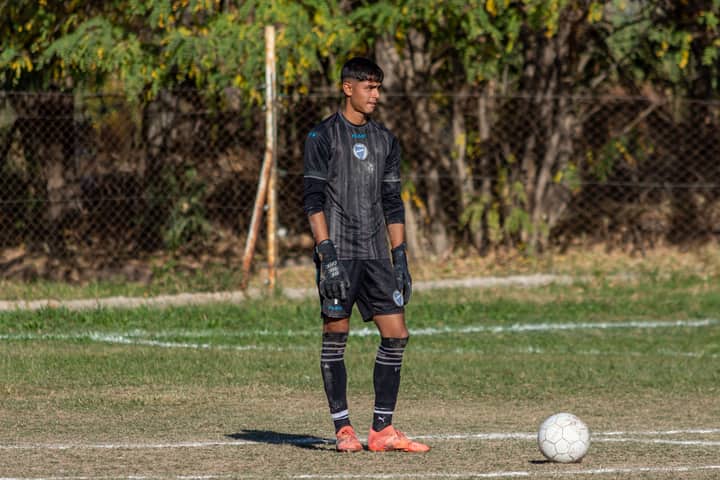 A focused young goalkeeper stands ready on the field during a sunny day soccer match.