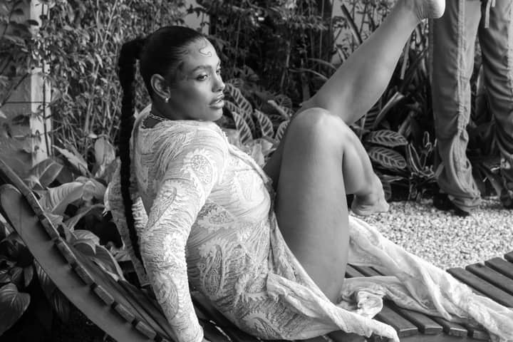 Stylish woman in lace dress posing outdoors on a chair in black and white.