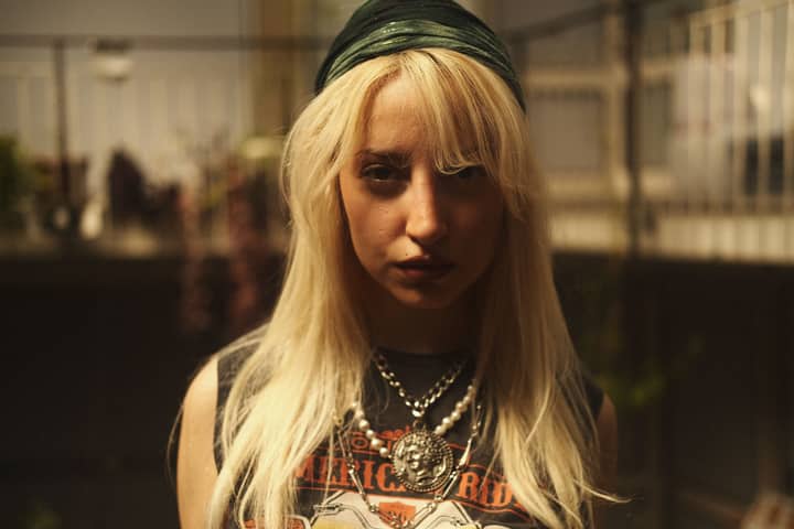 Blonde woman with retro necklace in urban setting, edgy fashion.