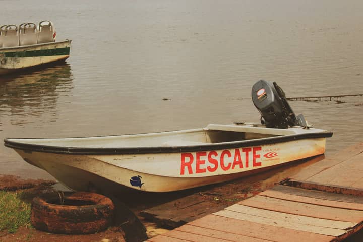 A rescue boat titled 'RESCATE' docked by a calm lakeside, ready for emergency use.