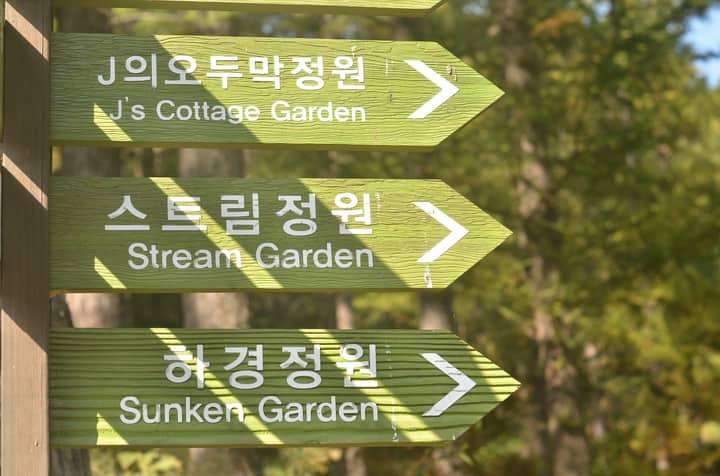 Directional signs point to different gardens in a tranquil Korean setting.