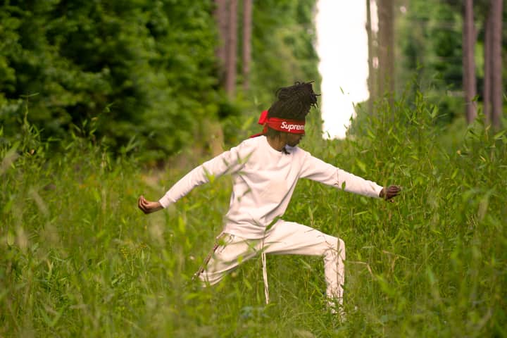 A person in a white tracksuit performing martial arts outdoors in a green forest.