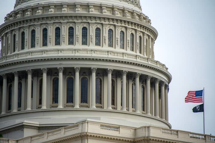 Detail of the US Capitol dome in Washington, D.C., featuring an American flag waving beside it.
