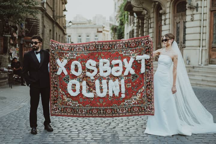 Stylish couple holds Azerbaijani carpet on cobbled street, embodying cultural elegance.