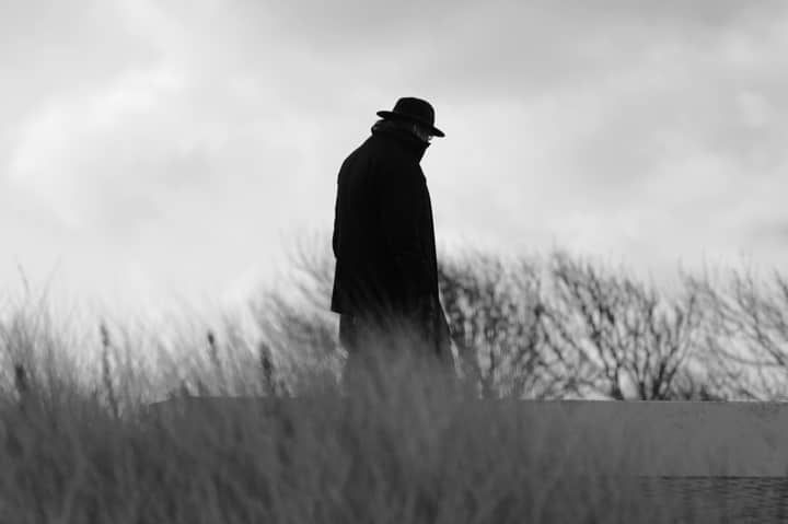 A black and white silhouette of a man walking in a winter landscape.