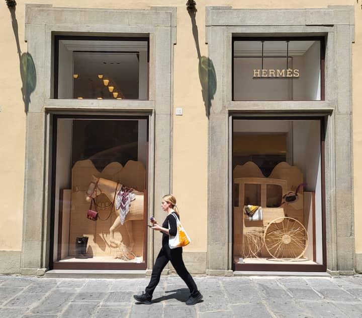 Fashion-conscious woman walks past an elegant Hermes store display.