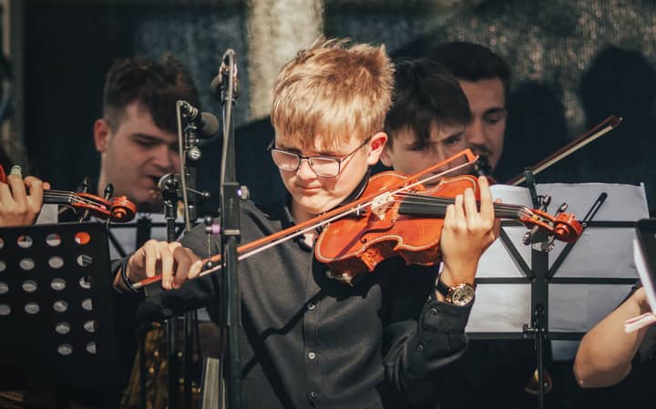 A young violinist passionately plays during an outdoor orchestra performance.