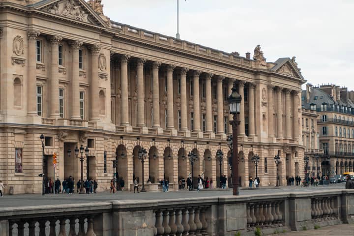 View of a neoclassical building facade in Paris with pedestrians walking below.