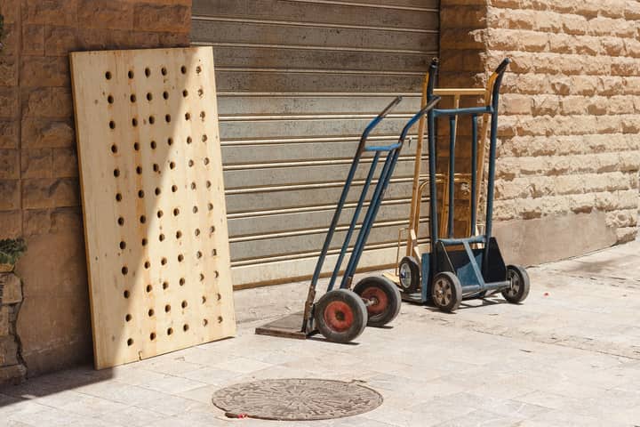 Hand trucks and perforated wooden panel in daylight against a brick wall on a sidewalk