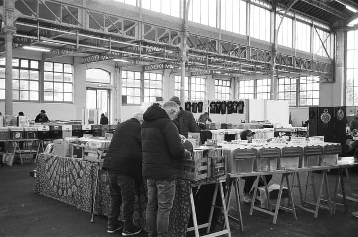 Black and white photo of a record fair in Nancy, capturing people browsing vinyl records indoors.