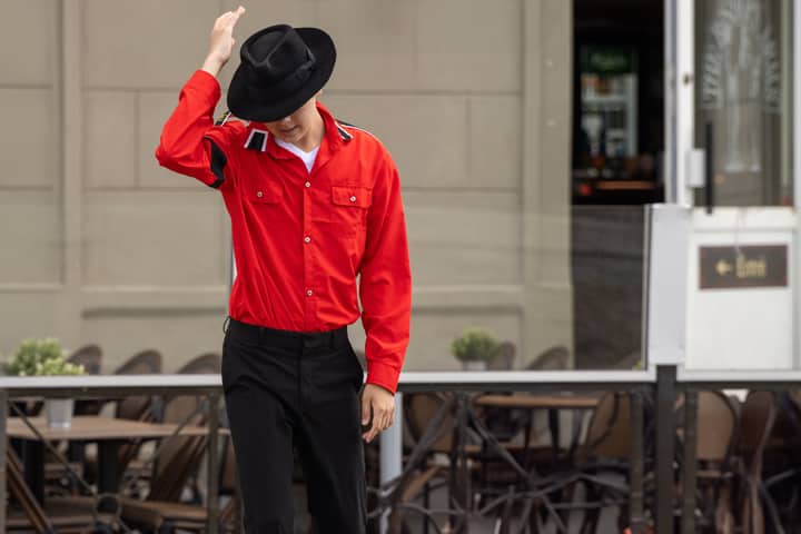 Young man in red shirt and hat adjusting his headgear outdoors in Paris.