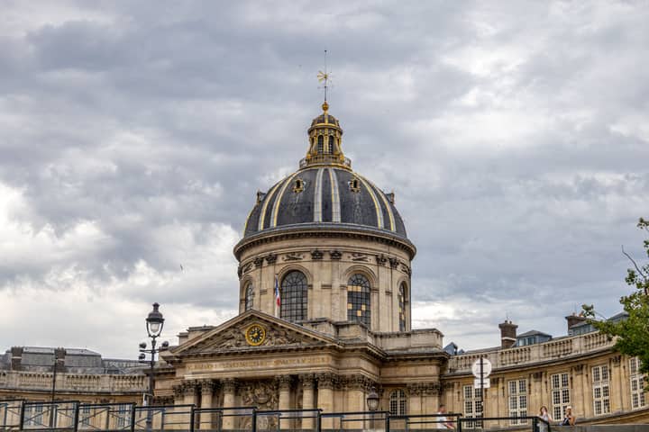 Architectural view of the iconic dome at the Institute of France in Paris under cloudy skies.