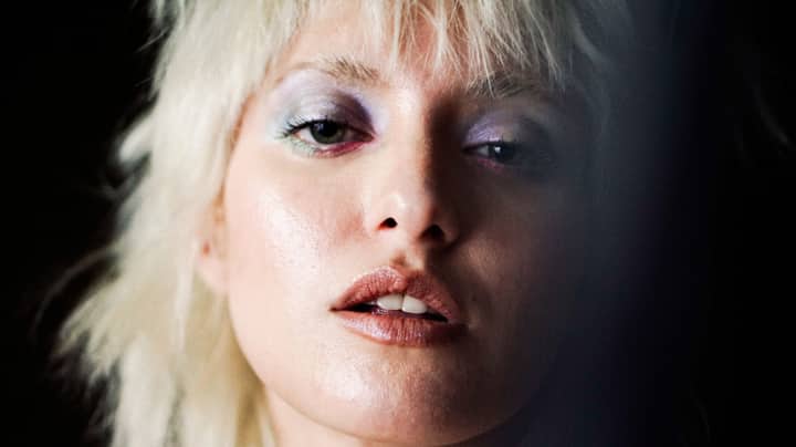 Artistic close-up portrait of a woman with blonde hair and vivid makeup, captured in moody lighting.